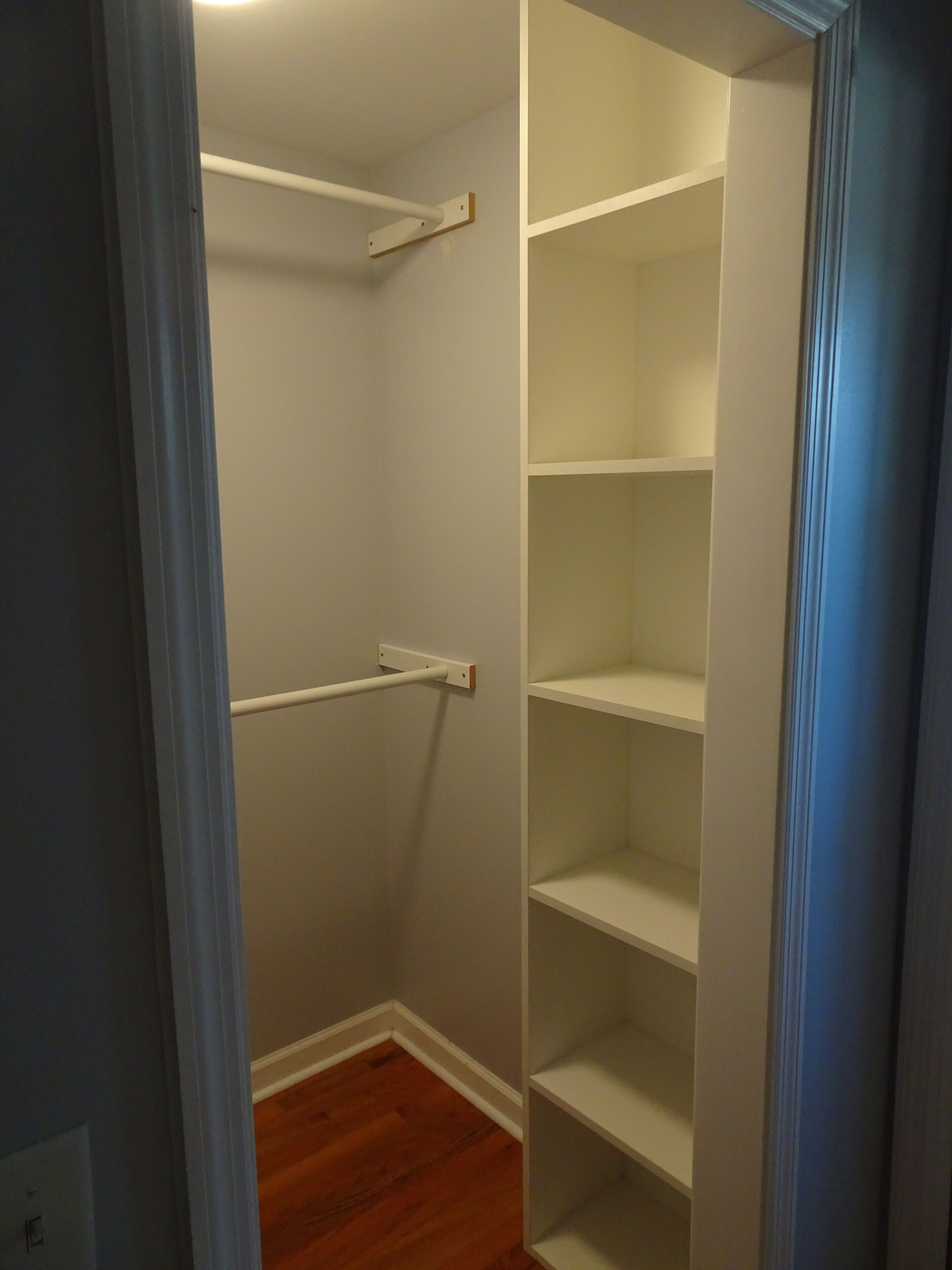 A walk-in closet with white shelving units and a wooden floor.