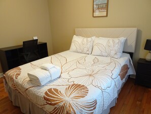 A neatly made bed with a floral bedspread, a bedside table with a lamp, and a wall with a motivational quote. - House in Savannah, Ga (Garden City)