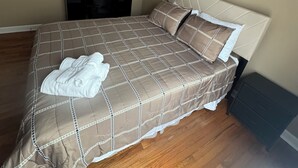 A bedroom with a bed, a ceiling fan, a nightstand, a painting, and a wooden floor.