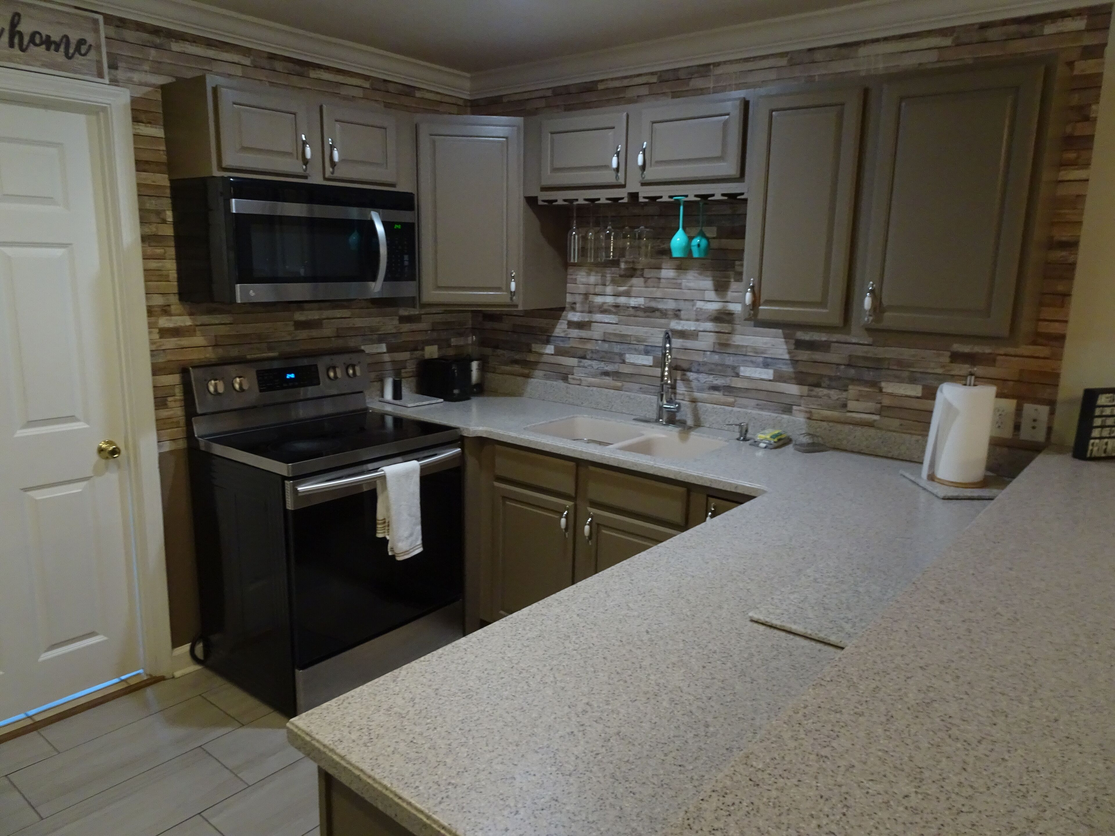 A kitchen with a stainless steel oven, a microwave, a sink, and a backsplash with a stone pattern.