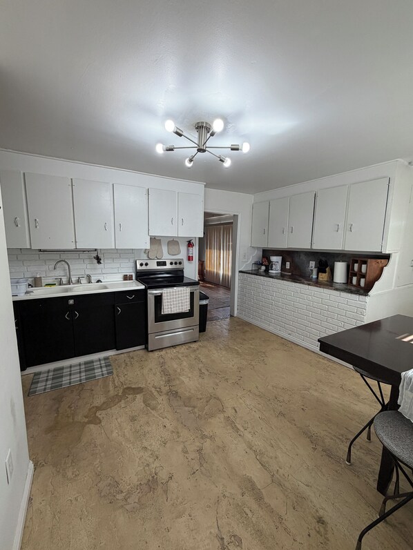 A kitchen with white cabinets, a black countertop, a stainless steel stove, and a black dining table.