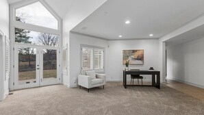 A spacious room with a large sliding glass door leading to an outdoor area, a comfortable sofa, a dining table with chairs, and a painting on the wall.
