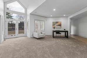 A spacious room with a large sliding glass door leading to an outdoor area, a comfortable sofa, a dining table with chairs, and a painting on the wall.