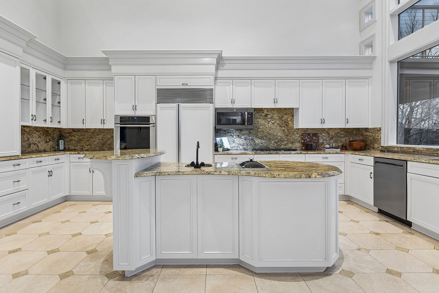 A spacious kitchen with white cabinetry, granite countertops, and a central island.