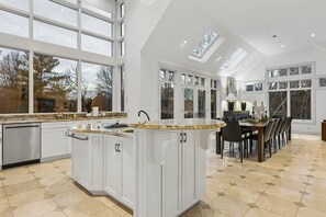 A spacious kitchen with a central island, large windows, and a dining area with chairs.