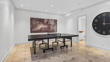 Une pièce avec une table de ping-pong, un grand tableau abstrait et une horloge murale ronde.
