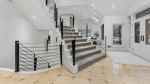 A modern staircase with a glass railing, leading to a landing with a door and a view of the outdoors.