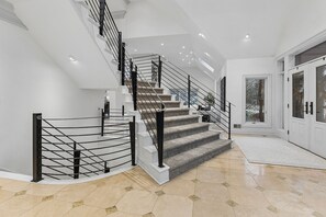 A modern staircase with a glass railing, leading to a landing with a door and a view of the outdoors.