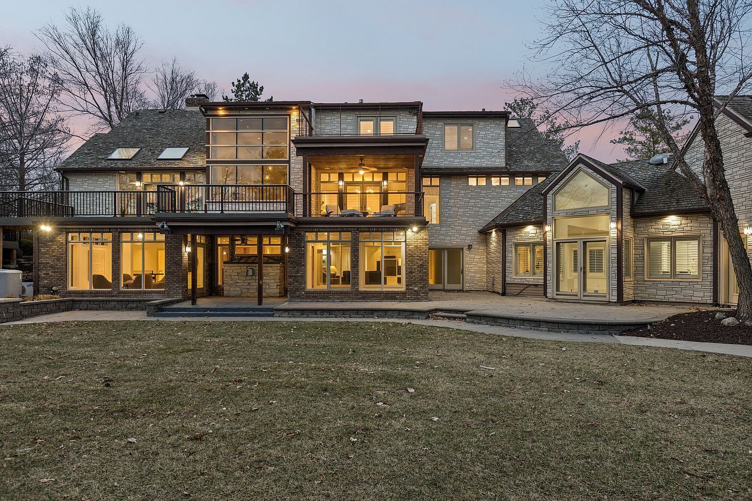 A multi-story house with a covered patio, large windows, and a well-maintained lawn.