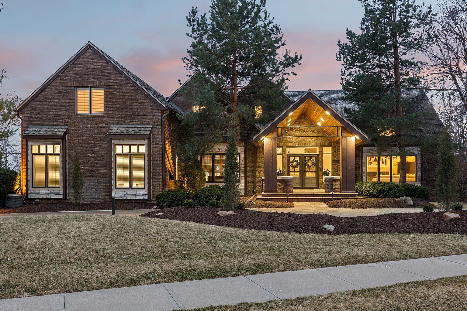 A two-story house with a brick exterior, a front porch with a bench, and a well-maintained lawn.