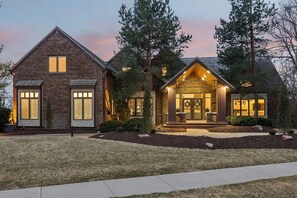 A two-story house with a brick exterior, a front porch with a bench, and a well-maintained lawn.