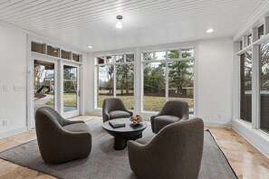 A room with a large glass door leading outside, a round table with chairs, and a view of a backyard with trees and a playground.