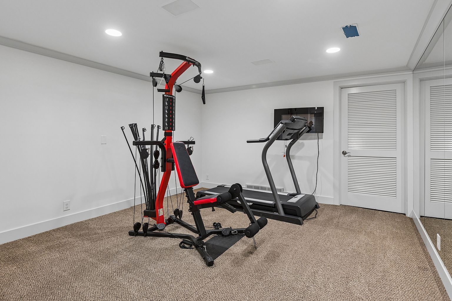 Une salle de sport à domicile équipée d’un vélo d’appartement, d’un banc de musculation et d’un appareil à câbles.