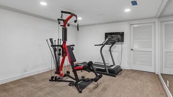 Une salle de sport à domicile équipée d’un vélo d’appartement, d’un banc de musculation et d’un appareil à câbles.