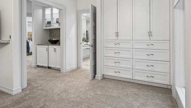A hallway with a white wardrobe, a kitchen area, and a mirrored closet door.