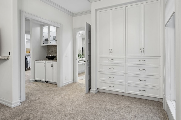 A hallway with a white wardrobe, a kitchen area, and a mirrored closet door.