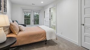 A bedroom with a bed, a nightstand, a lamp, and a view of the outdoors through a sliding door.