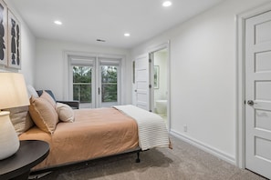 A bedroom with a bed, a nightstand, a lamp, and a view of the outdoors through a sliding door.