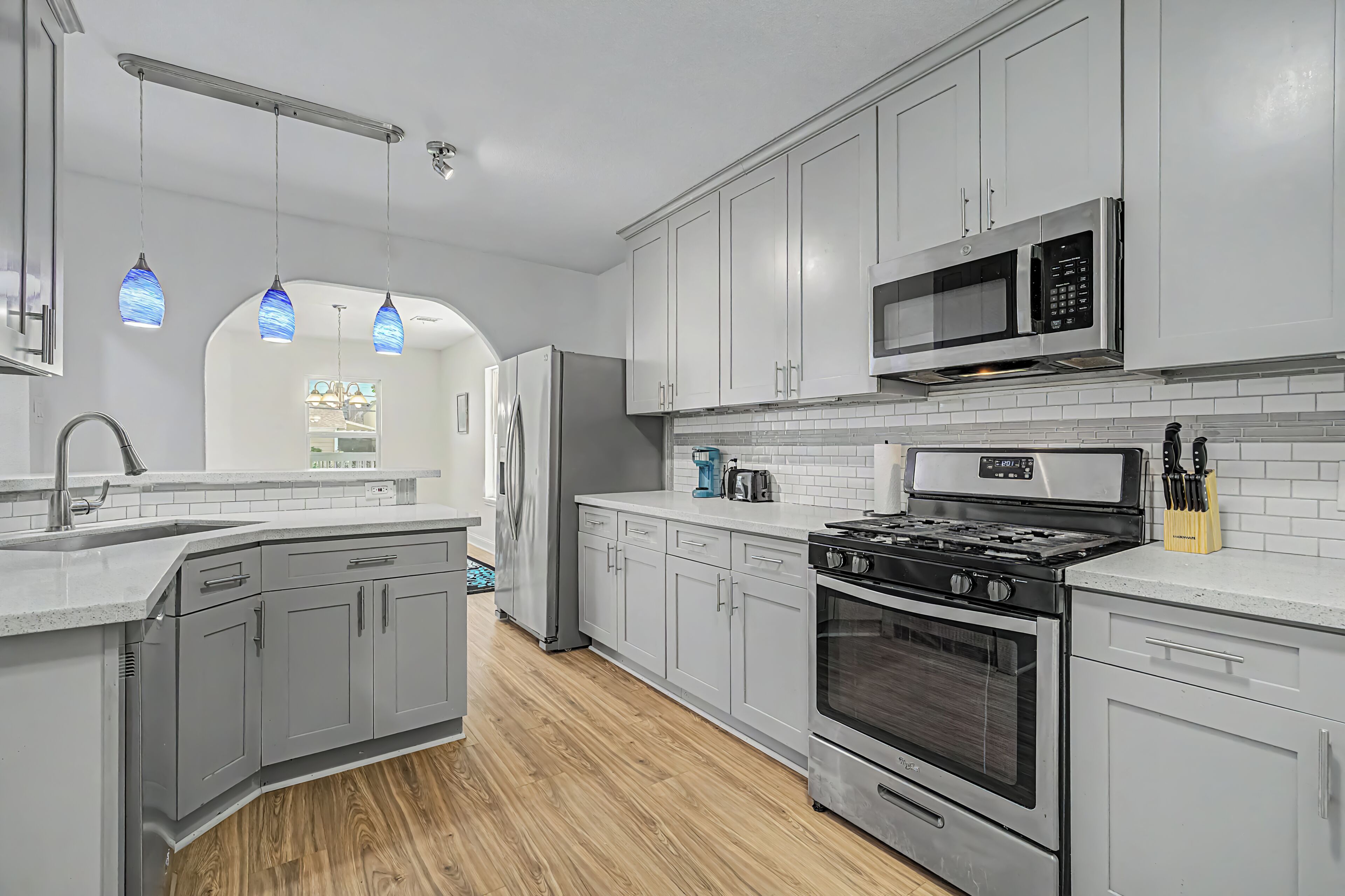 A modern kitchen with stainless steel appliances, white cabinetry, and a wooden floor.