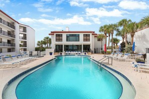 A swimming pool with lounge chairs and a building with balconies. - 🧜🏻‍♀️Ocean Front Complex | Ocean Views | Pet Friendly | Las Brisas 523🧜🏻‍♀️ (New Smyrna Beach)