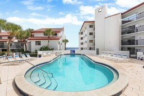 Una piscina con lettini e palme, circondata da edifici con balconi.