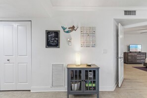 Una habitación con puerta cerrada, un termostato en la pared, un adorno mural, una estantería con una lámpara y un televisor sobre un aparador.
