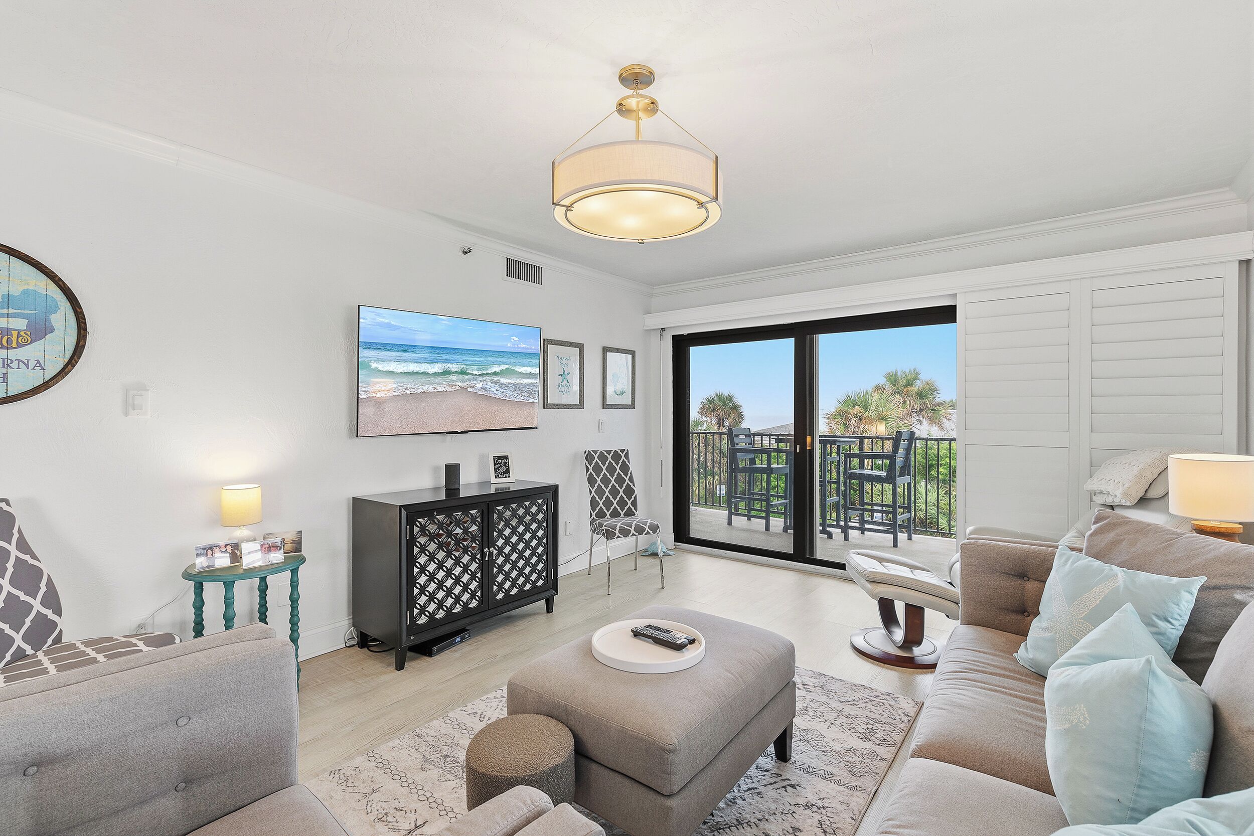 A living room with a large TV, a sofa, a coffee table, and a view of the outdoors through a sliding door.