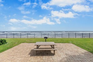 Un tavolo da picnic su una superficie pavimentata, con vista sull'oceano e una recinzione metallica sullo sfondo.