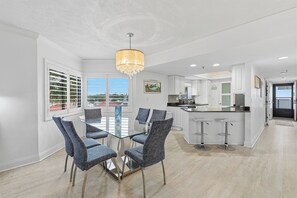 Una cocina moderna con armarios blancos, una isla central con taburetes y un comedor con mesa de vidrio y sillas.