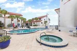 Zona de piscina con jacuzzi, sillas de descanso y palmeras.