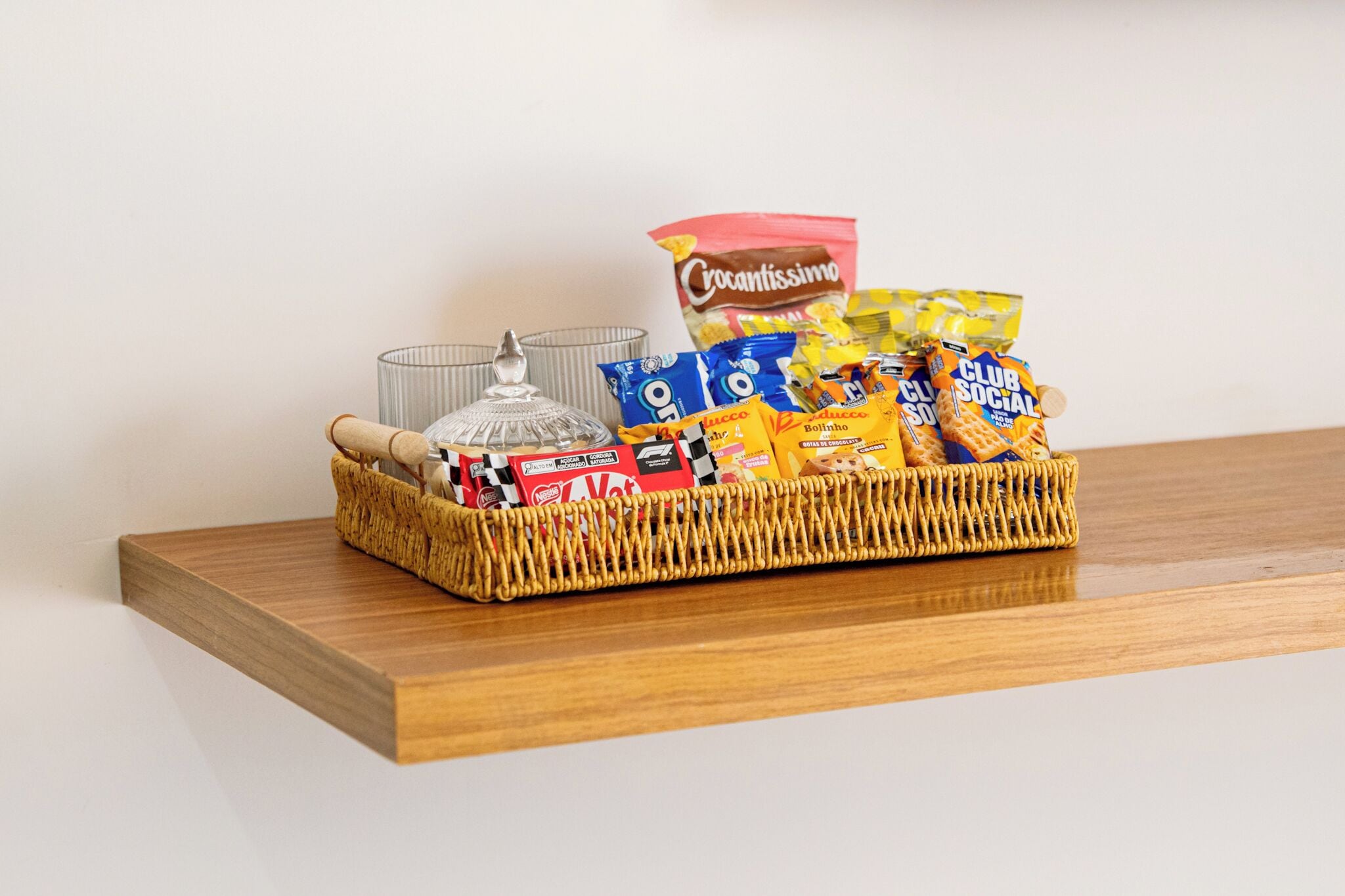 A wicker basket filled with snacks and a glass container on a wooden shelf.