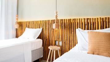 Quarto de hotel com duas camas, cabeceira de madeira, um banquinho pequeno e luminária pendente.