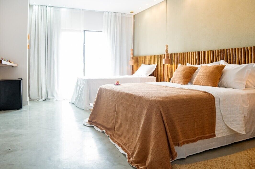 Habitación de hotel con dos camas, un ventanal grande con cortinas, cabecera de madera y televisor de pantalla plana.