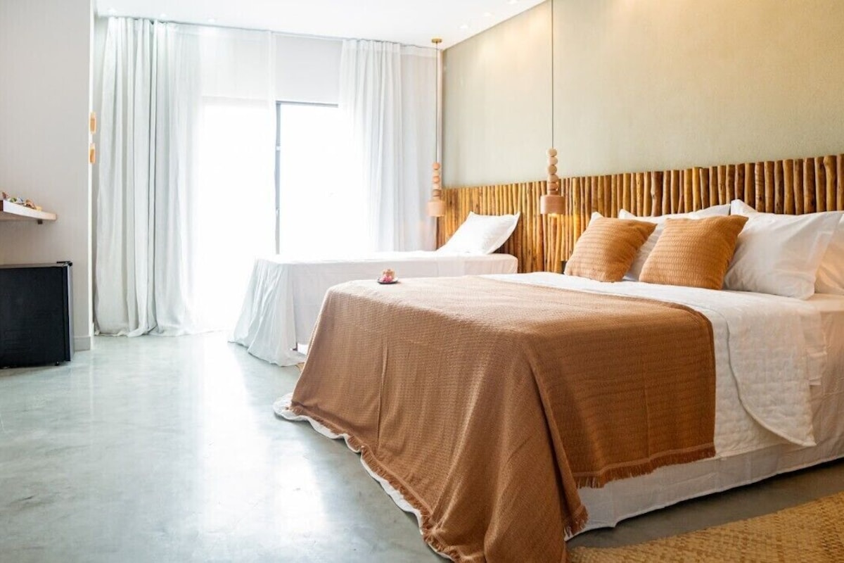 Habitación de hotel con dos camas, un ventanal grande con cortinas, cabecera de madera y televisor de pantalla plana.