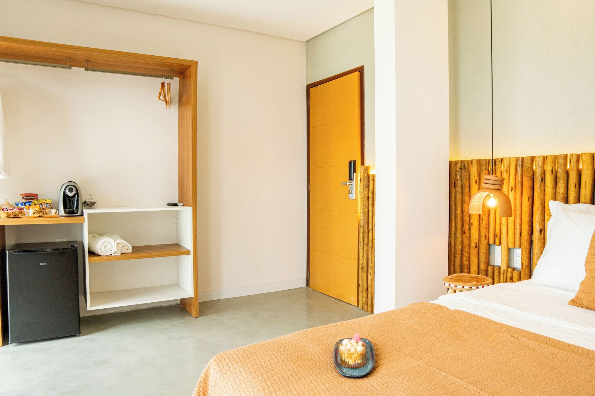 A hotel room with a bed, a desk, a chair, a small refrigerator, and a door.