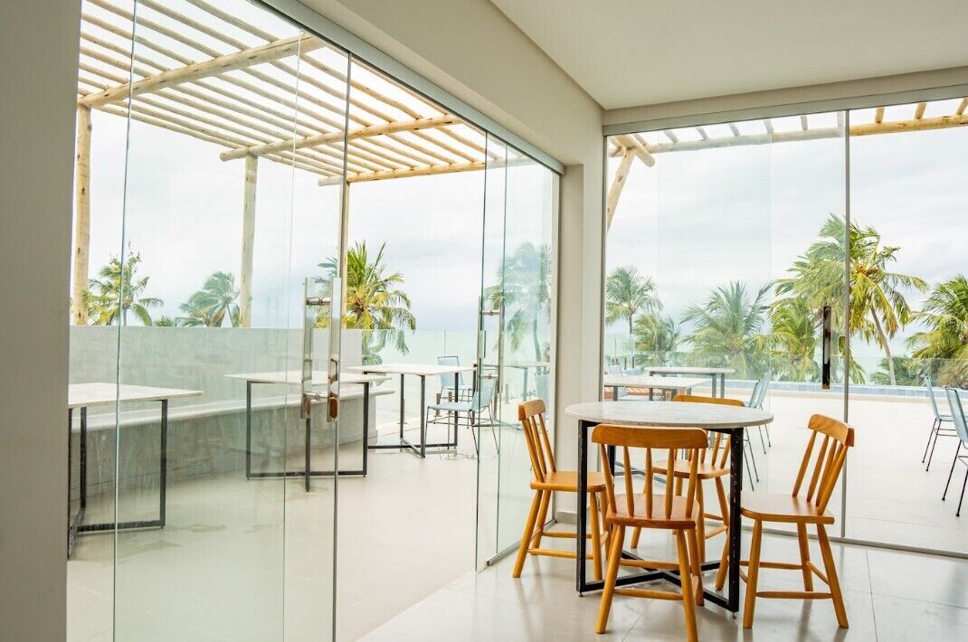 Un espacio moderno para comer al aire libre con paredes de vidrio y mobiliario de madera, con vistas a un paisaje tropical.