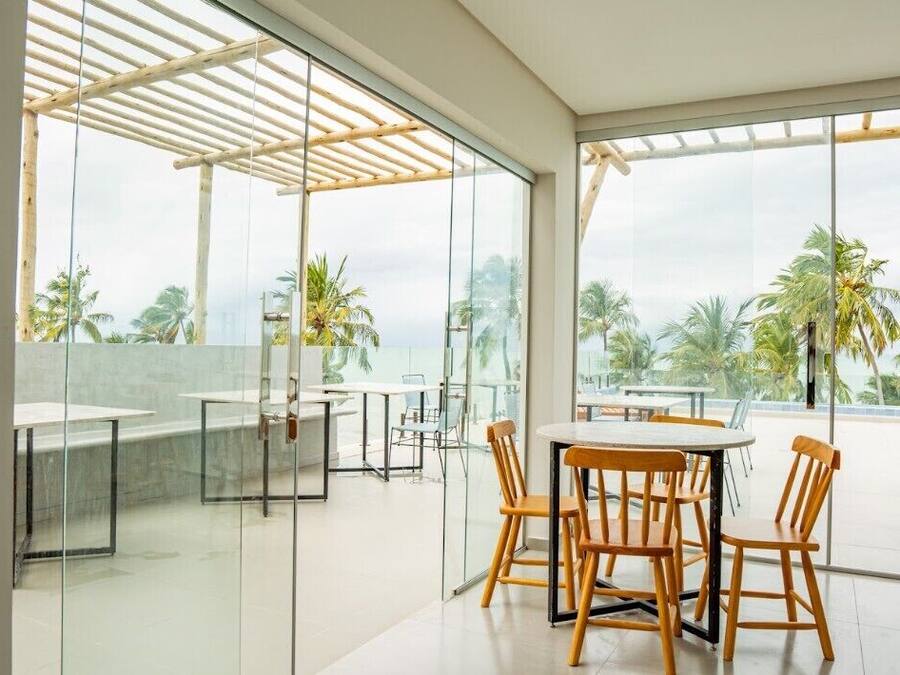 A modern outdoor dining area with glass walls and wooden furniture, overlooking a tropical landscape.