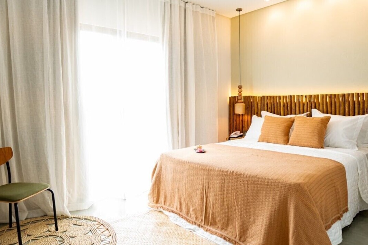 Una habitación de hotel con una cama, una silla, una mesita de noche y una lámpara.