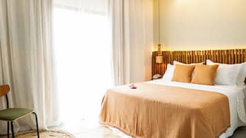 A hotel room with a bed, a chair, a bedside table with a lamp, and a view of the outdoors through sheer curtains.