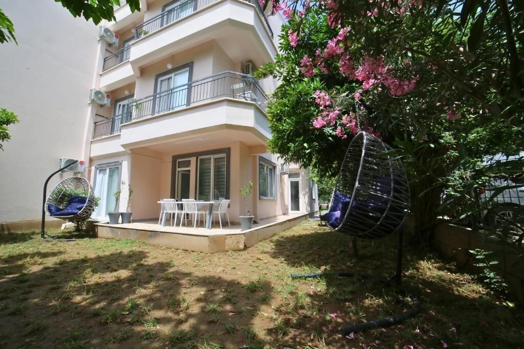 A two-story residential building with a balcony, outdoor seating, and a tree with pink flowers.