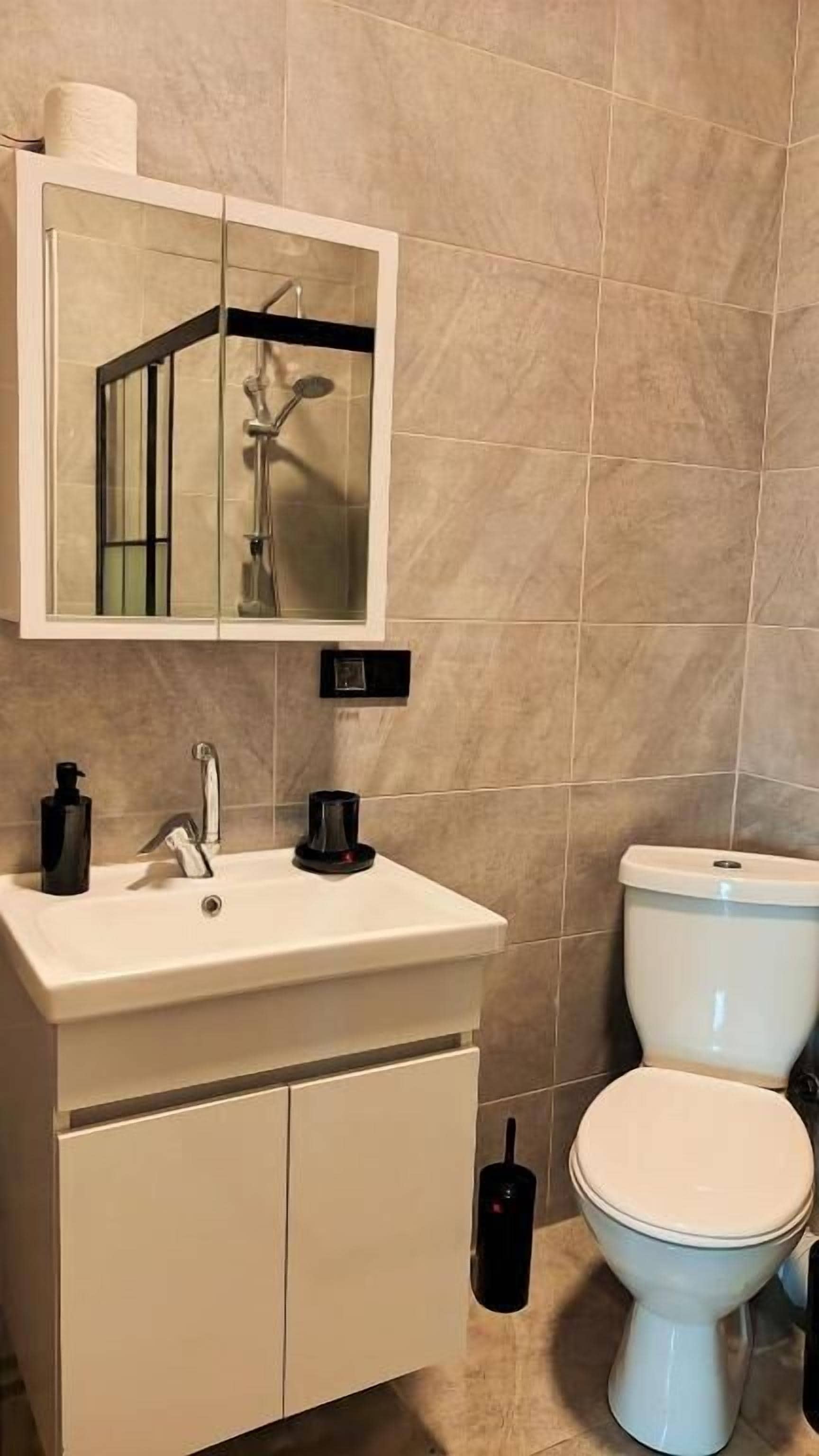 Un baño con un lavamanos blanco, un espejo encima, un inodoro y un bidé negro.
