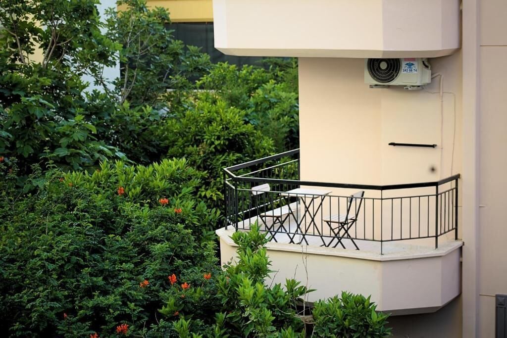 A balcony with a metal railing, surrounded by lush greenery and flowering plants.