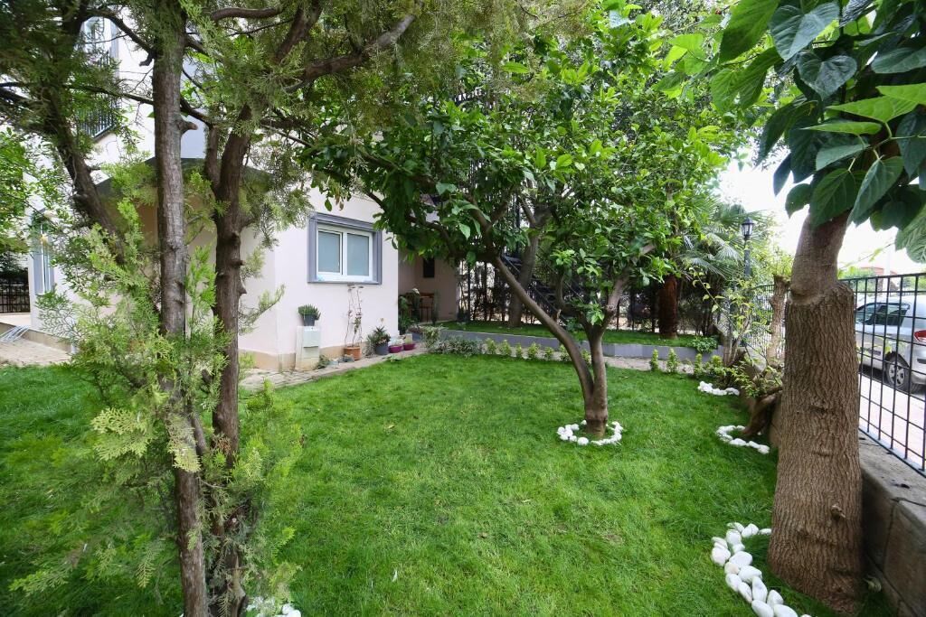 A well-maintained garden with a lawn, trees, and a white building with a window.