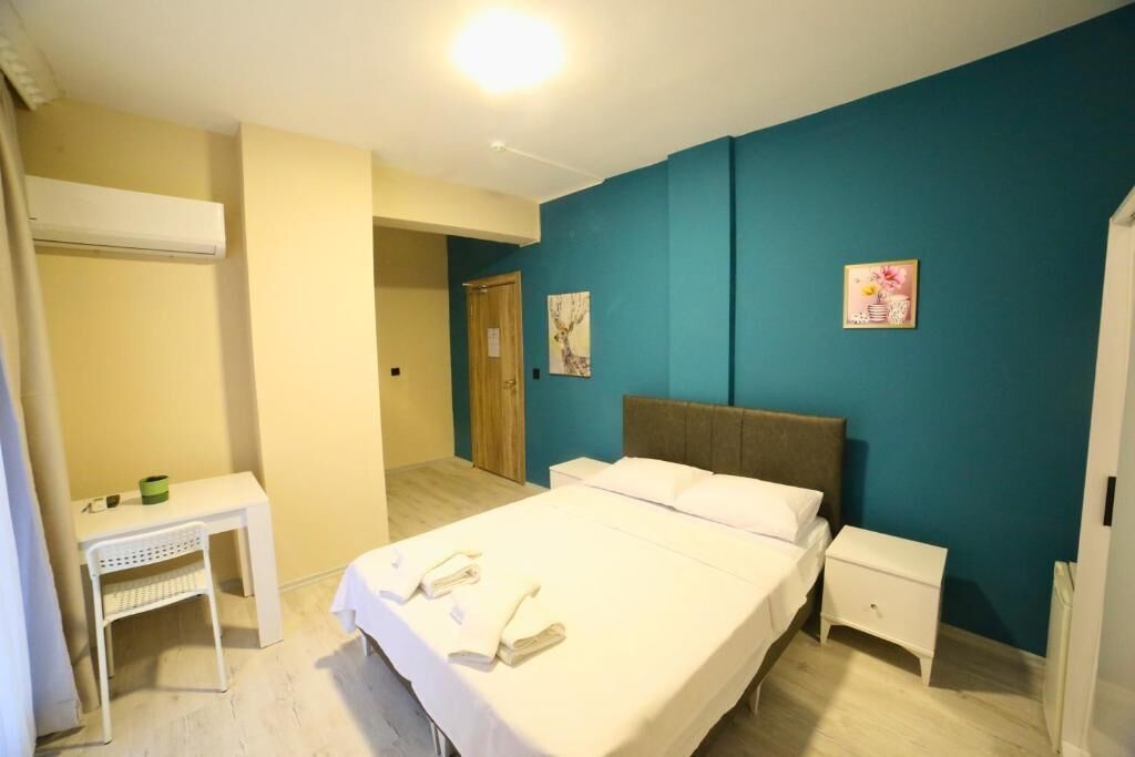 A bedroom with a bed, bedside tables, a desk, and a chair. There is a door leading to another room.