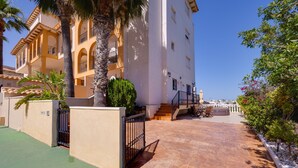 A residential building with a courtyard, a staircase leading to an upper level, and a view of the sea in the background. - Victoria Playa Campoamor (Orihuela)