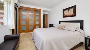 A bedroom with a bed, a bench, a painting, and a door with frosted glass panels. - Victoria Playa Campoamor (Orihuela)