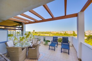Ein Balkon mit Korbmöbeln, einem Glastisch und Topfpflanzen.