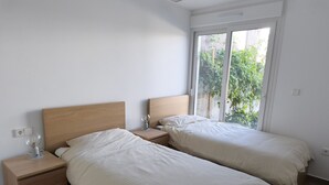 Ein Schlafzimmer mit zwei Betten, einem Nachttisch mit Lampe und einem Fenster mit Blick ins Grüne.