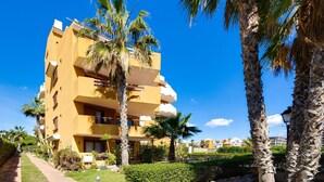 A multi-story hotel with balconies, palm trees, and a clear blue sky. - Recoleta Penthouse Punta Prima (Torrevieja)
