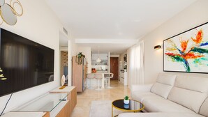 A modern living room with a flat-screen TV, a sofa, a coffee table, and a dining area in the background. - Recoleta Penthouse Punta Prima (Torrevieja)
